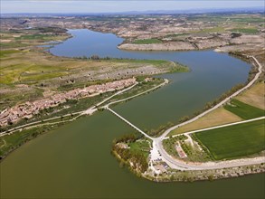 An aerial view of a wide landscape with a river flowing past a village and cultivated fields,