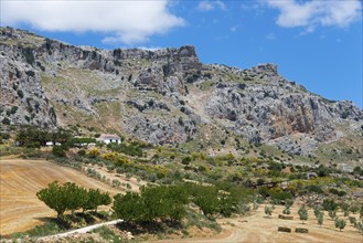 Barren rocky landscape with a small farmhouse surrounded by fields under a clear sky, nature