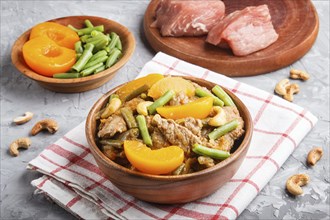 Fried pork with peaches, cashew and green beans on a black concrete background. side view, close