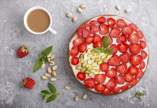 Homemade cake with yoghurt cream, strawberry, pistachio and a cup of coffee on a gray concrete