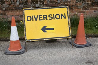 Yellow rectangular diversion sign with arrow pointing standing by two traffic cones, UK