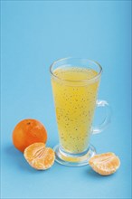 Glass of tangerine orange colored drink with basil seeds on a blue background. Morninig, spring,