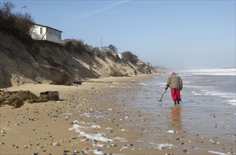 Male detectorist using metal detector walking along sandy beach Hemsby, Norfolk, England, UK