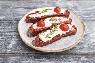 Red beet bread sandwiches with cream cheese and tomatoes on gray wooden background. Side view,