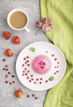 Pink mousse cake with strawberry and a cup of coffee on a gray concrete background and green