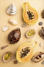 Ripe cut papaya, passion fruit, seashells, pebbles on orange pastel background. Top view, flat lay,