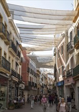 Fabric spread over buildings to provide shade in busy shopping street in central Seville, Spain,