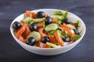 Vegetarian salad of tomatoes, cucumbers, parsley, olives and mustard on black wooden background,