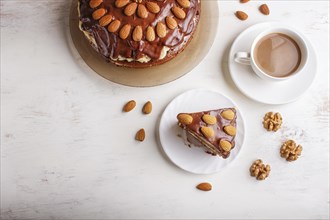 Homemade chocolate cake with milk cream, caramel and almonds on white wooden background. cup of