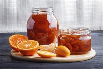 Tangerine and kumquat jam in a glass jar on a black wooden table and white linen background.