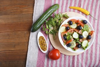 Vegetarian salad of tomatoes, cucumbers, parsley, olives and mustard on linen tablecloth, top view,