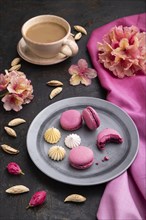 Purple macarons or macaroons cakes with cup of coffee on a black concrete background and pink