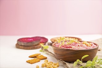 Hummus with beet and microgreen basil sprouts in wooden bowl on a white and pink background and