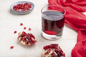 Glass of pomegranate juice on a white concrete background with red textile. Side view, close up