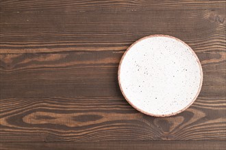 Empty white with dots ceramic plate on brown wooden background. Top view, copy space, flat lay