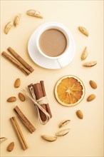 Composition with almonds, cinnamon and cup of coffee on orange pastel background. Blank, flat lay,