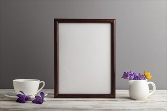 Brown wooden frame mockup with snowdrop crocus flowers and white coffee cup on gray paper