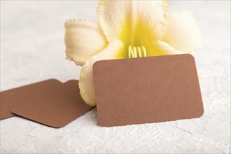 Brown paper business card mockup with orange day-lily flower on gray concrete background. Blank,