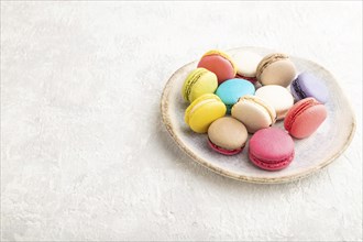 Multicolored macaroons on ceramic plate on gray concrete background. side view, close up, still