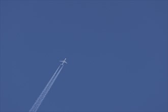 Jet aircraft flying across a blue sky leaving a contrail or vapor trail in the atmosphere behind