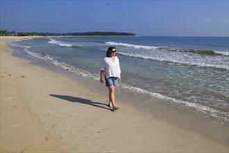 Ocean and woman walking on sandy tropical beach at Pasikudah Bay, Eastern Province, Sri Lanka, Asia