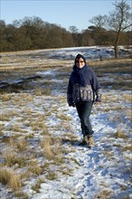 Front view of model released mature woman standing in heathland with covering of snow, Suffolk,