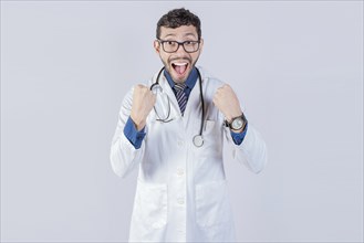 Young doctor is happy celebrating something, he is wearing glasses and stethoscope, he is looking