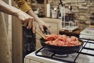 Unrecognizable man stirring chopped chicken fillet in frying pan with wooden spatula