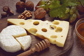 Cheese with big holes, emmental, maasdam, brie cheese, on a cutting board, with grapes and honey,