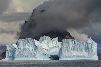 Large icebergs in fjord in front of steep mountains, cloudy mood, summer, Scoresby Sound, East