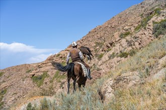 Traditional Kyrgyz eagle hunter with eagle in the mountains, hunting on horseback, near Kysyl-Suu,