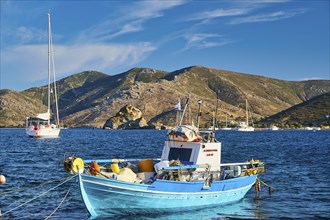 Colourful fishing boat on blue water, with mountains and cloudy sky in the background, Petras