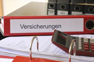 Symbolic image: Folder with insurance policies and calculator on a desk