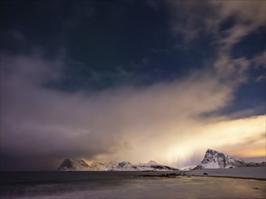 Snow-capped mountains on the coast at night, starry sky and clouds, Vestvagoy Island, Lofoten,