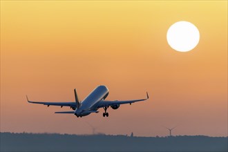 An aeroplane flies in the sunrise sky, surrounded by intense orange tones, passenger plane after