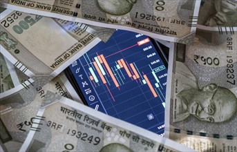 Stock market graph or chart display on a mobile phone against Indian 500 rupee paper currency note