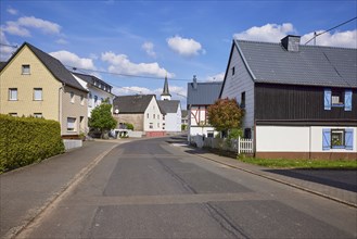 Street with houses under a blue sky with cumulus clouds in Beuren, Eifel, district of Cochem-Zell,