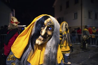 Person with detailed mask and yellow cloak at night, carnival, Schellbronn night parade,