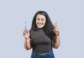 Happy young woman holding toothbrush pointing up. Smiling girl holding toothbrush and pointing up