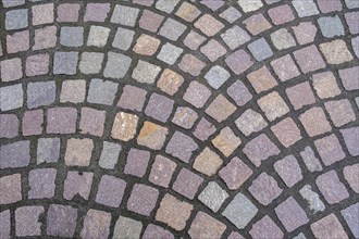 Pavement made of irregularly arranged, square paving stones in shades of grey, purple and brown,