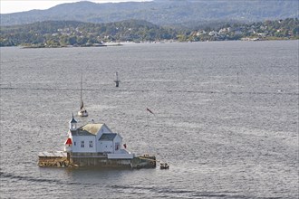 A lighthouse, restaurant in the sea with a small sailing boat and a hilly landscape in the