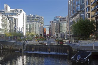 Urban scene with modern buildings and a canal with small, artificial waterfalls and boats, capital,