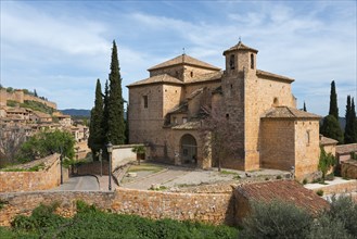 A medieval stone church surrounded by cypress trees in a tranquil Mediterranean landscape under a