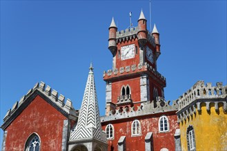 Red tower with clock and architectural decorations under a blue sky, detail, Palácio Nacional da