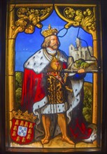 Depiction of a king with crown and mantle in front of a castle, in a medieval stained glass window,