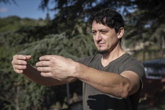 A Caucasian man adopts the Tree Hugging Posture during his Qi Gong training session. Rooted in