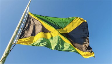 The flag of Jamaica flutters in the wind, isolated against a blue sky