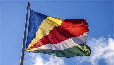 The flag of Seychelles, fluttering in the wind, isolated against a blue sky