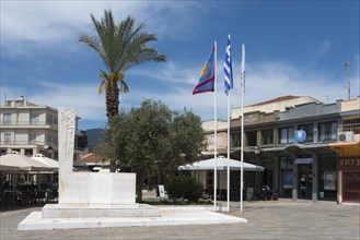 A town square with a monument surrounded by palm trees, flags and a café, 23 March Square with a