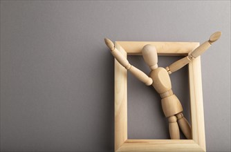 Wooden mannequin climbs out of a wooden frame with raised arms on gray pastel background. escape,